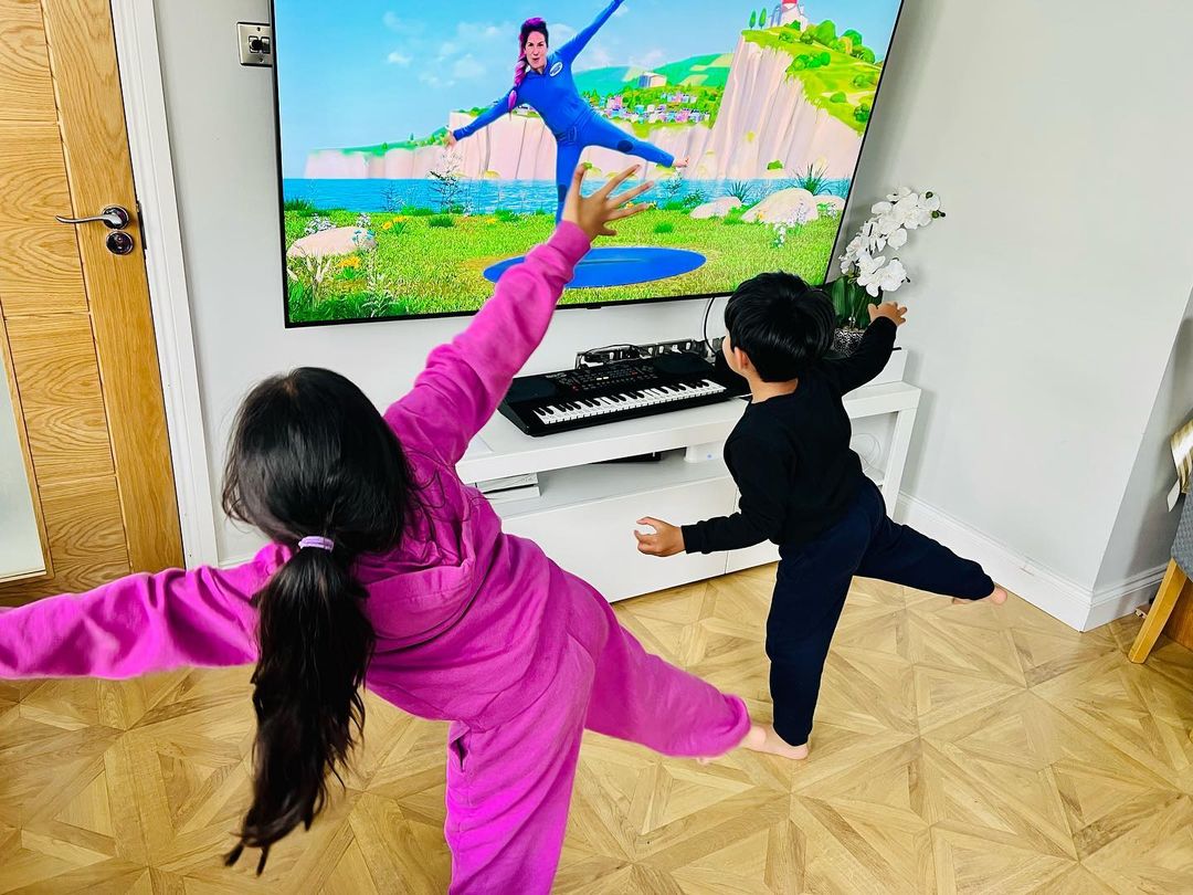 Children doing yoga in front of the TV with Cosmic Kids on screen